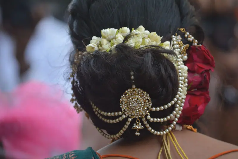 Close-up of a bride's hair bun adorned with jasmine flowers, pearls, and gold ornaments.