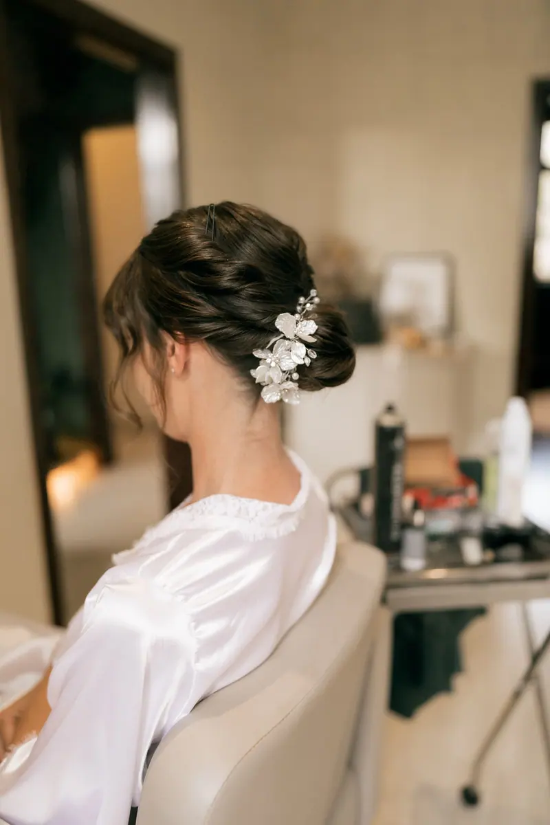 Back view of bride with elegant updo hairstyle and floral accessory in a salon setting.