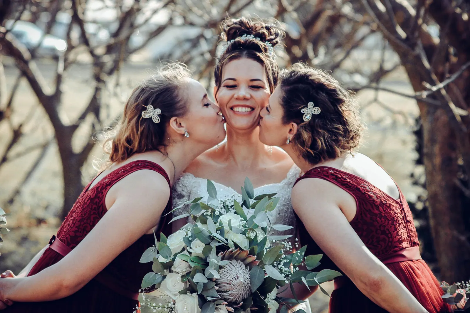 Bride and bridesmaids sharing a joyful moment outdoors with elegant floral bouquet.