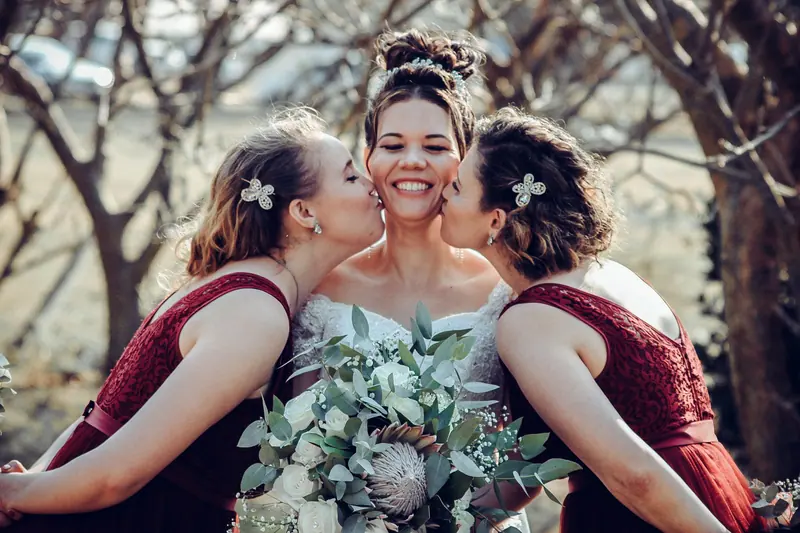 Bride and bridesmaids sharing a joyful moment outdoors with elegant floral bouquet.