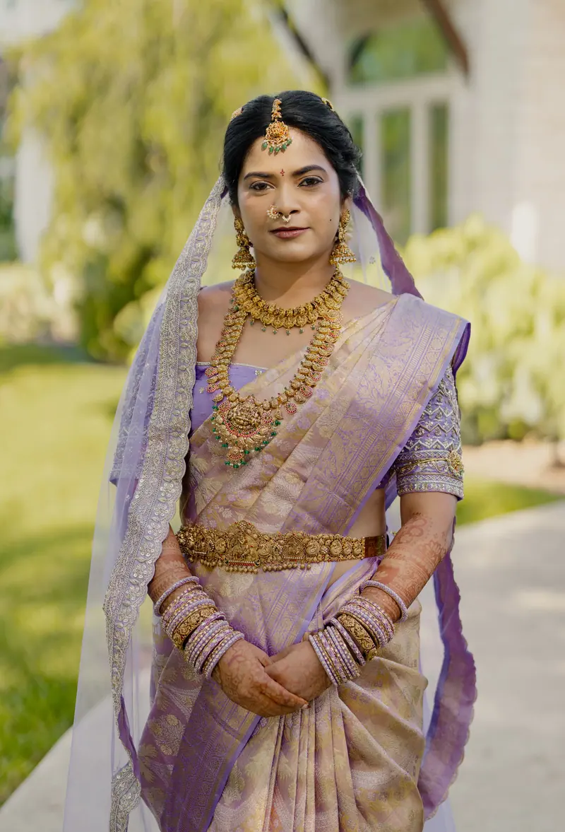 An elegant portrait of a South Asian bride in traditional attire, adorned with gold jewelry, outdoors.