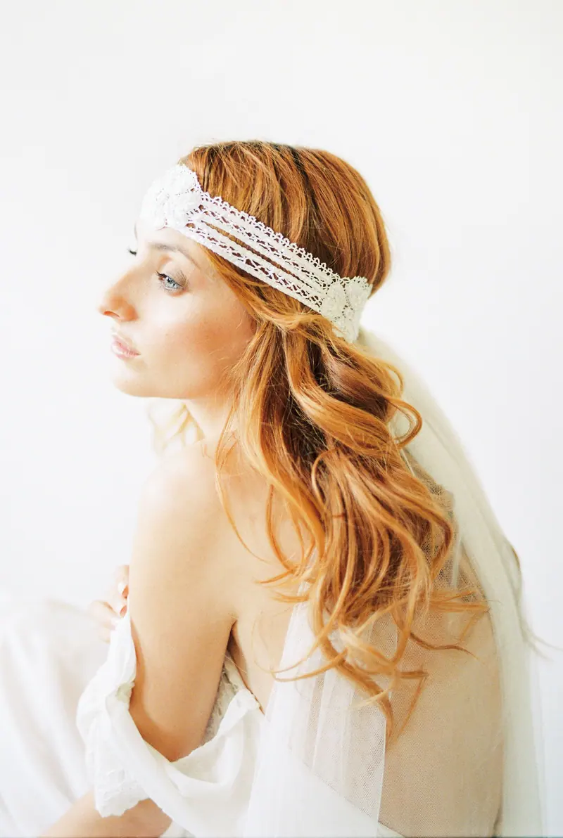 Captivating bridal portrait featuring a woman with red hair and lace headband, against a white background.
