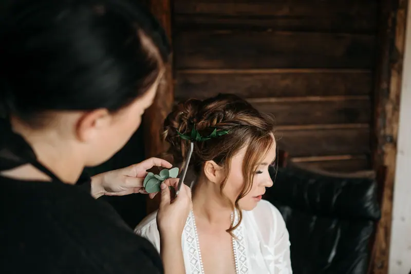 Elegant wedding hairstyle creation with intricate floral accents in a rustic setting.