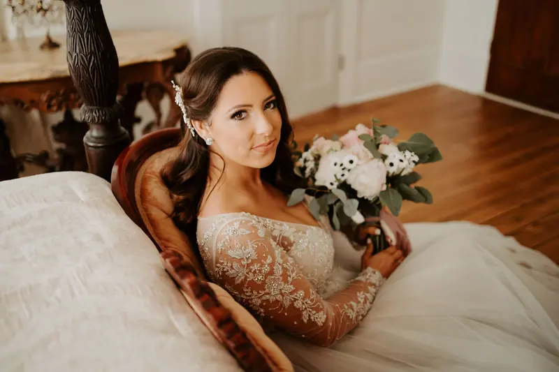 A beautiful bride in a lace gown holding a bouquet at an indoor wedding setting.