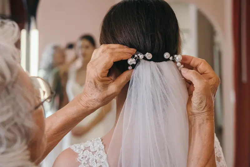 An elderly woman adjusts a bride's veil in a heartwarming pre-wedding moment.