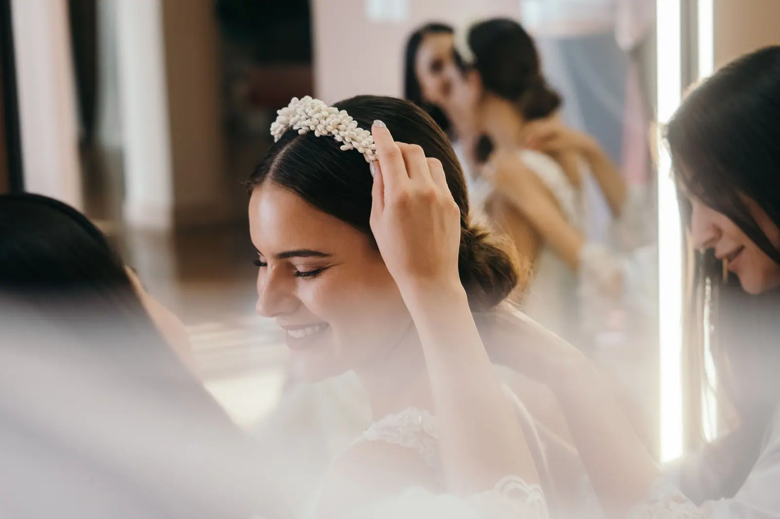 Bride with bridesmaids adjusting headband and preparing for wedding ceremony.