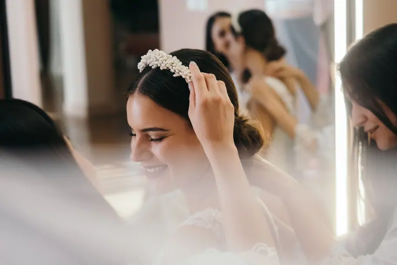Bride with bridesmaids adjusting headband and preparing for wedding ceremony.