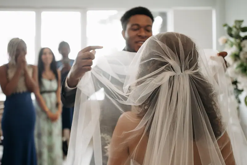 A groom lifting the bride's veil with guests watching at a wedding ceremony.