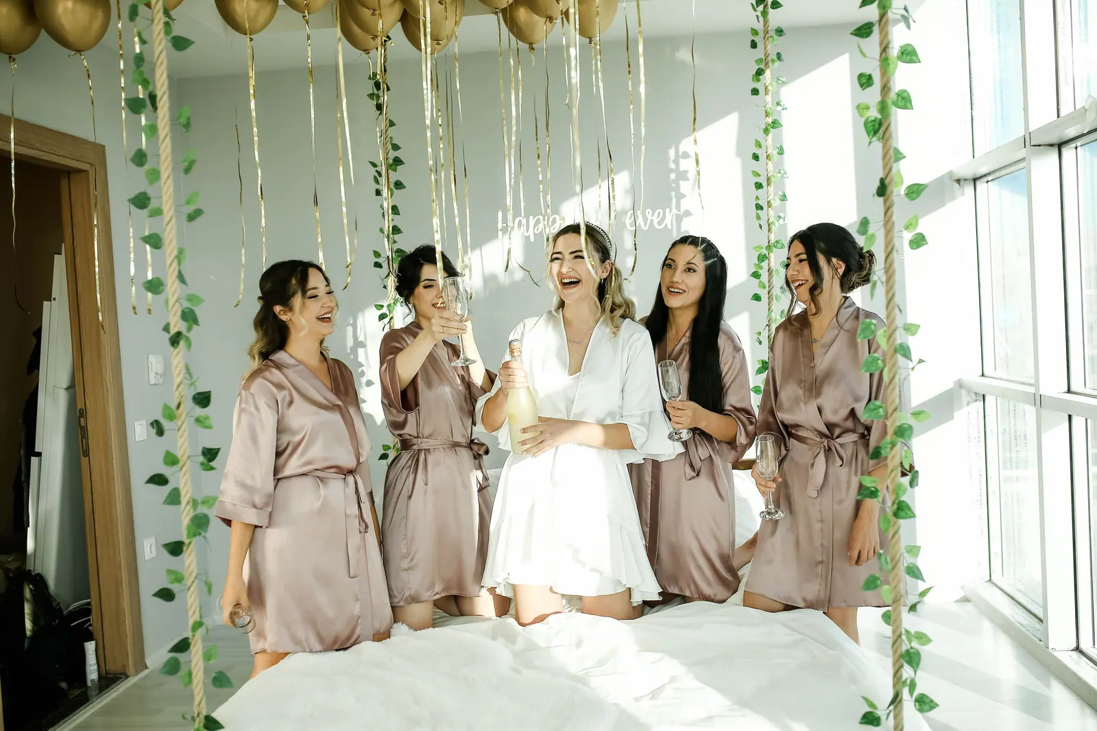 Bride and bridesmaids celebrating with champagne indoors. Joyful wedding preparation moment.