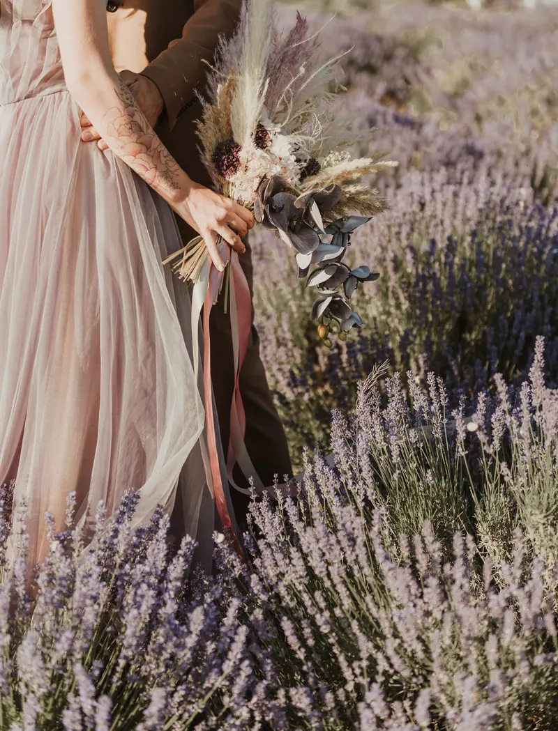 A couple holding hands with a bouquet in a lavender field, symbolizing love and romance.