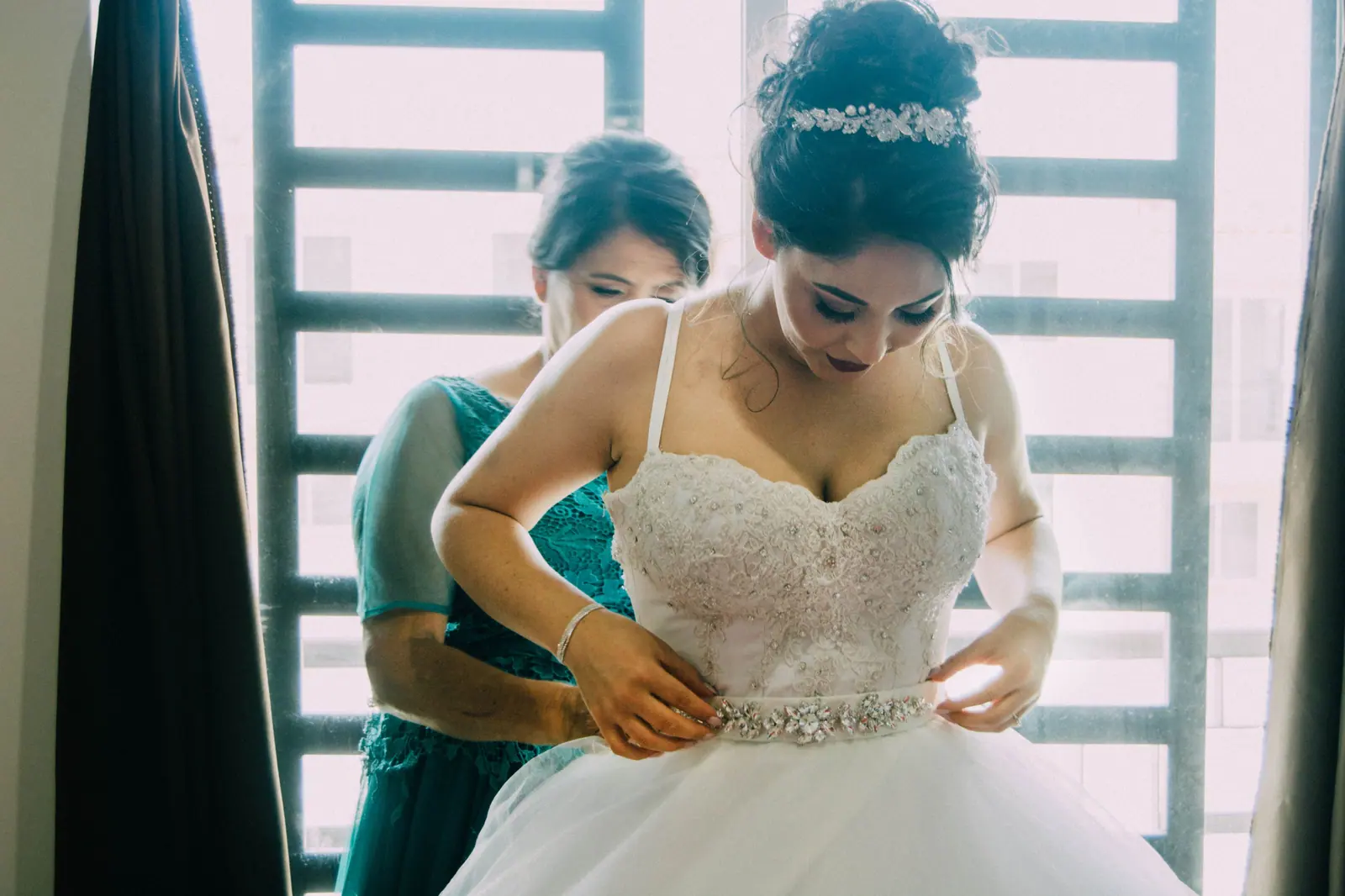A bride adjusting her dress with the help of a woman before her wedding ceremony.