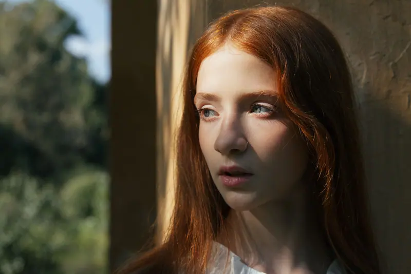 Thoughtful young redhead woman in sunlight creating a serene and contemplative mood.