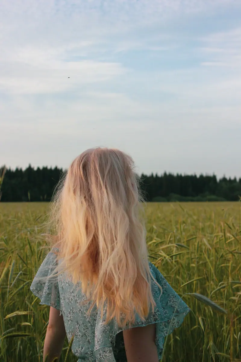 A blonde woman photographed from behind in a lush summer field.