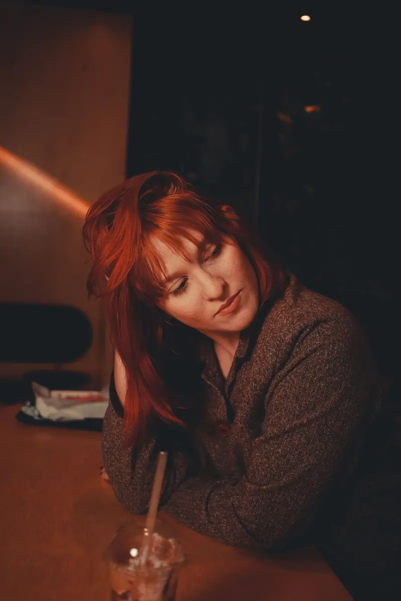 Charming redhead woman in a cafe, enjoying a relaxed moment with a drink.