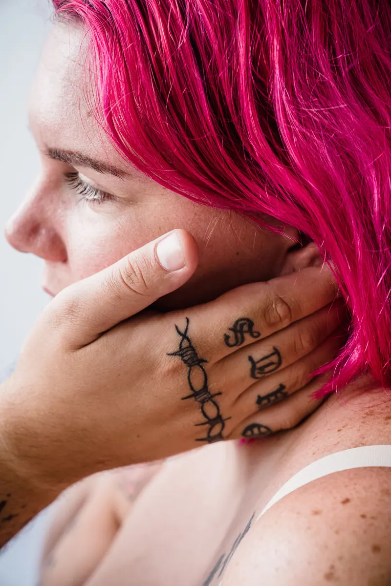 Artistic portrait showing a woman with vibrant pink hair and tattooed hand.