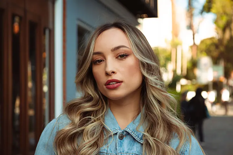 A fashionable woman with curly hair wearing a denim shirt outdoors.