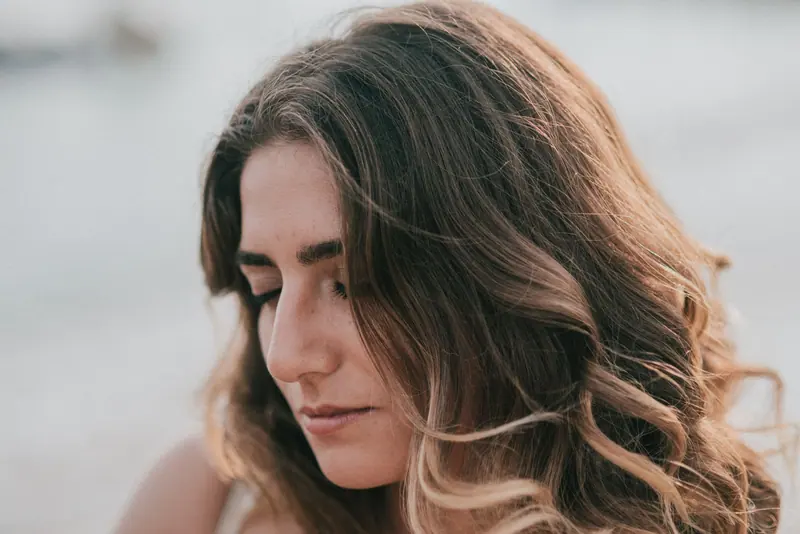 Close-up portrait of a young woman with wavy blonde hair and eyes closed, conveying serenity.