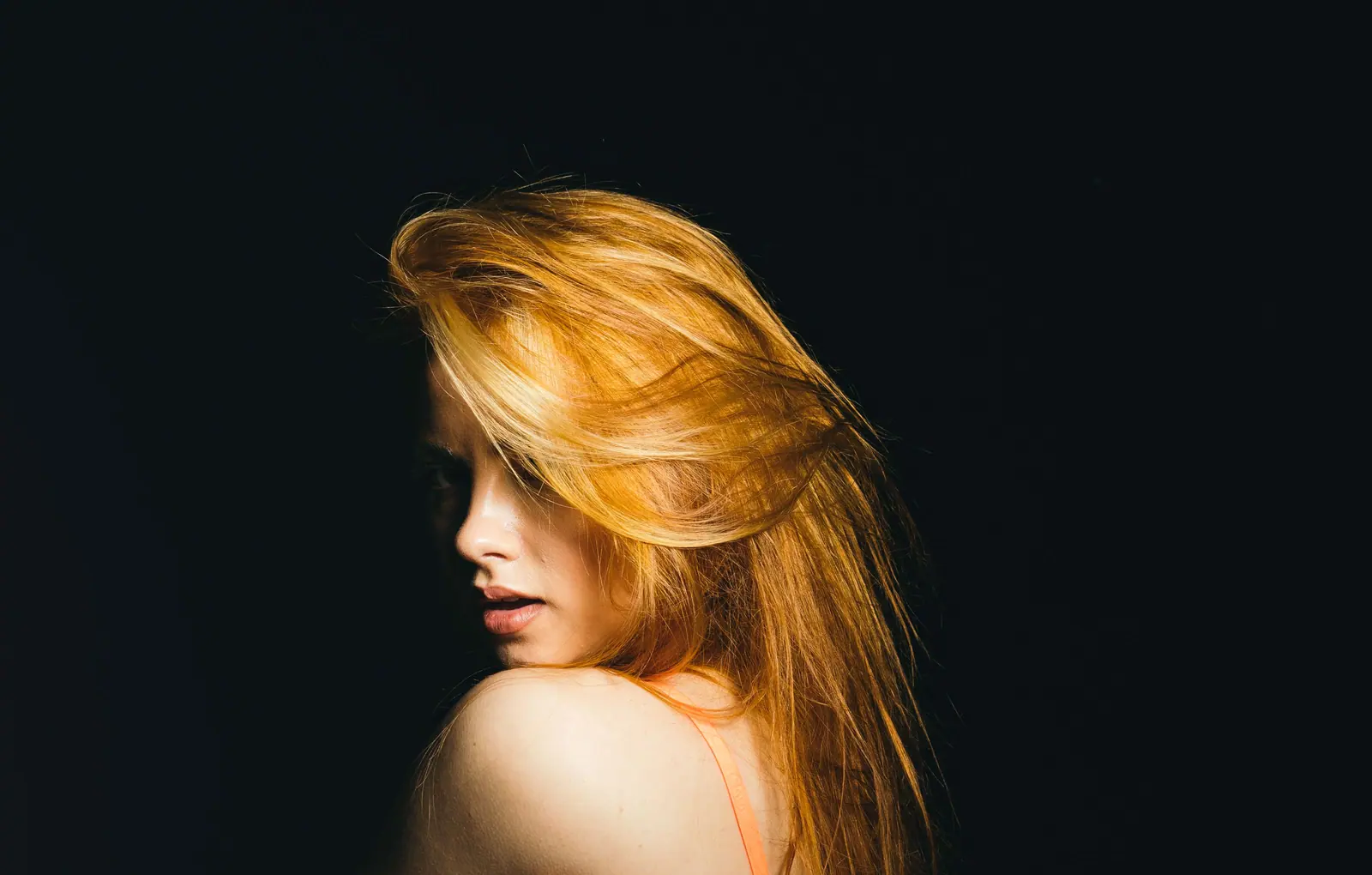Woman with long golden-blonde hair glowing against a black background