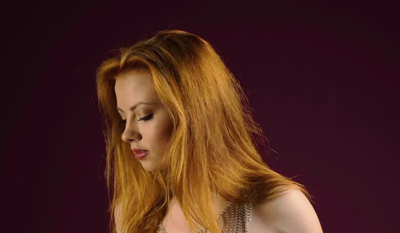 A serene and elegant portrait of a woman with flowing auburn hair against a dark backdrop.