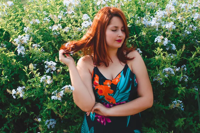 A red-haired woman in a floral dress enjoys a sunny day among blooming flowers.