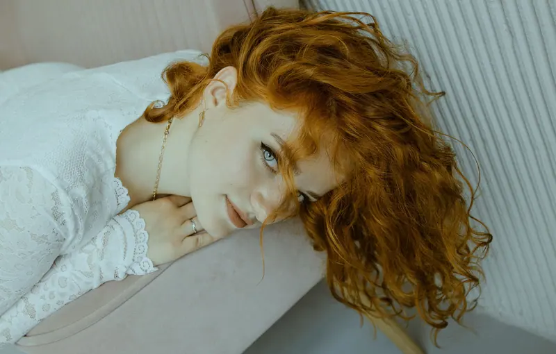 Woman with copper curls resting her head on her arm