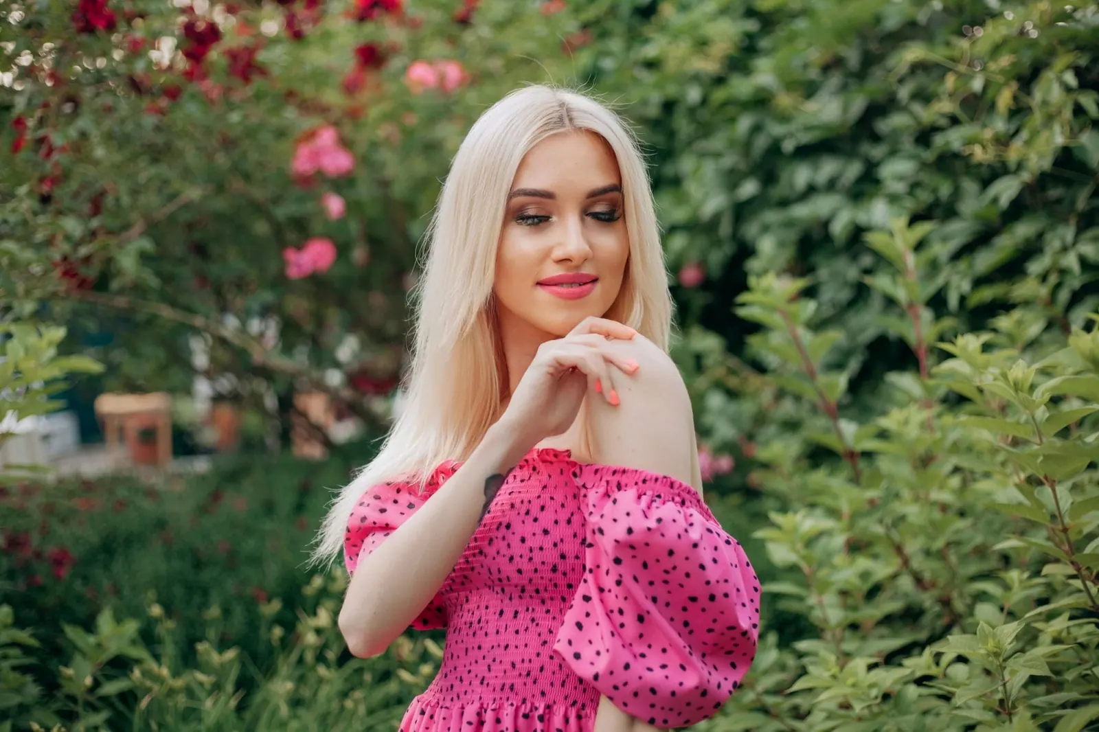 Platinum blonde in a pink polka-dot dress smiling among roses