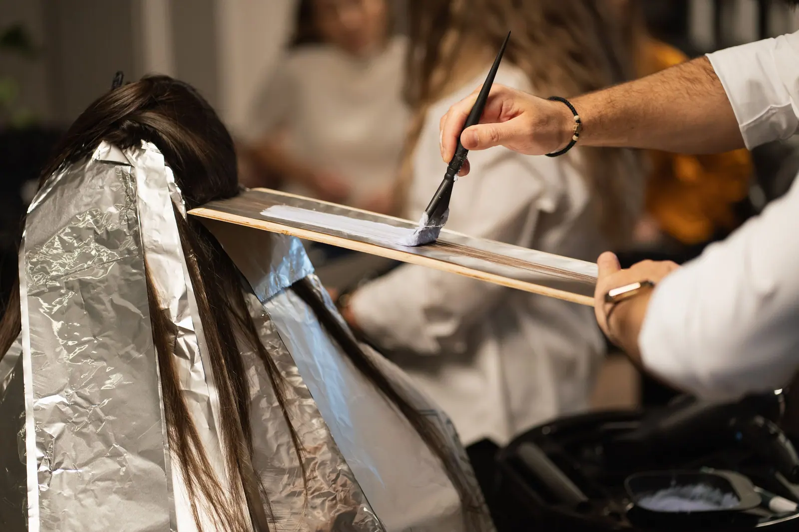 Colorist painting a foil section with her brush raised in a cinematic salon