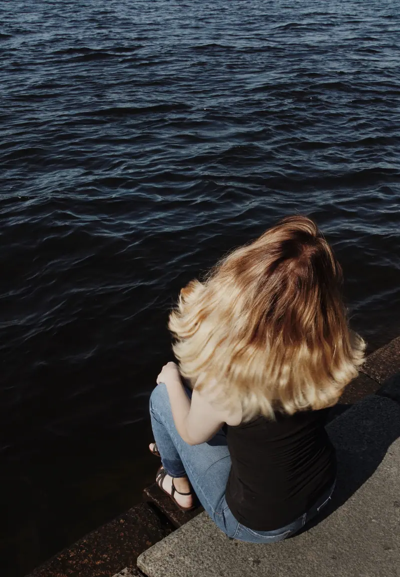 Blonde woman in jeans sitting by the water on a sunny day