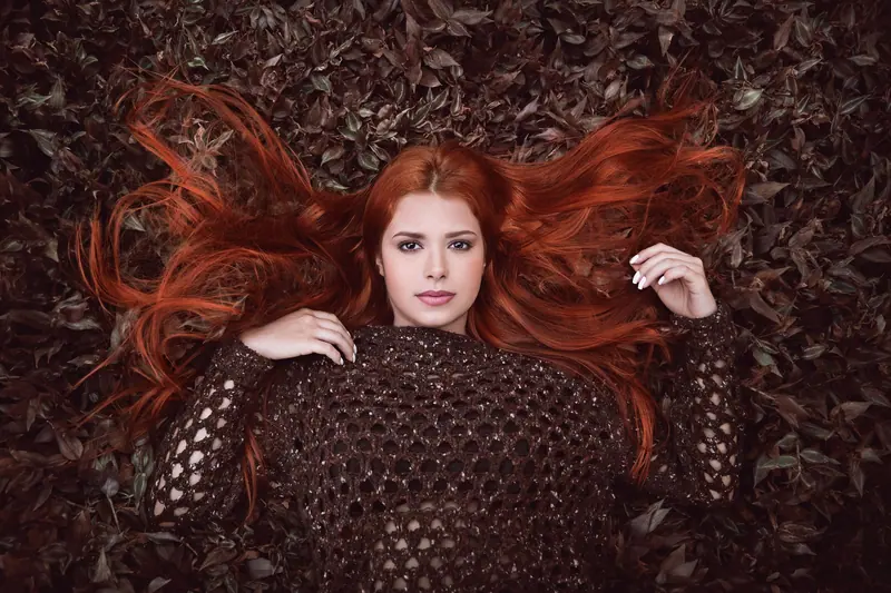 Portrait of a stylish redhead woman posing on fall leaves, exuding elegance and charm.