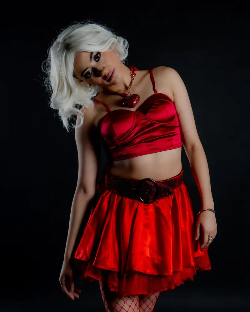 Chic woman with platinum hair in a vibrant red dress posed against a black background.