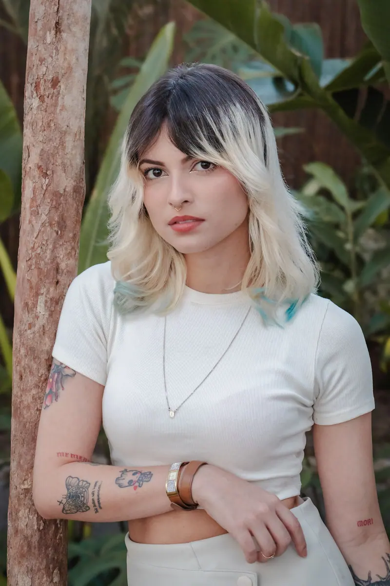 Young woman with tattoos posing outdoors in a tropical setting, showcasing her unique style.