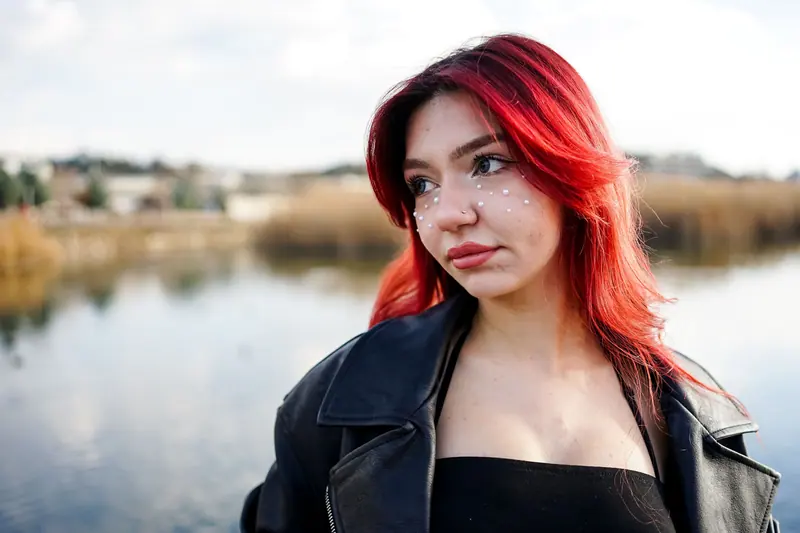Woman with crimson-and-black hair beside a lake
