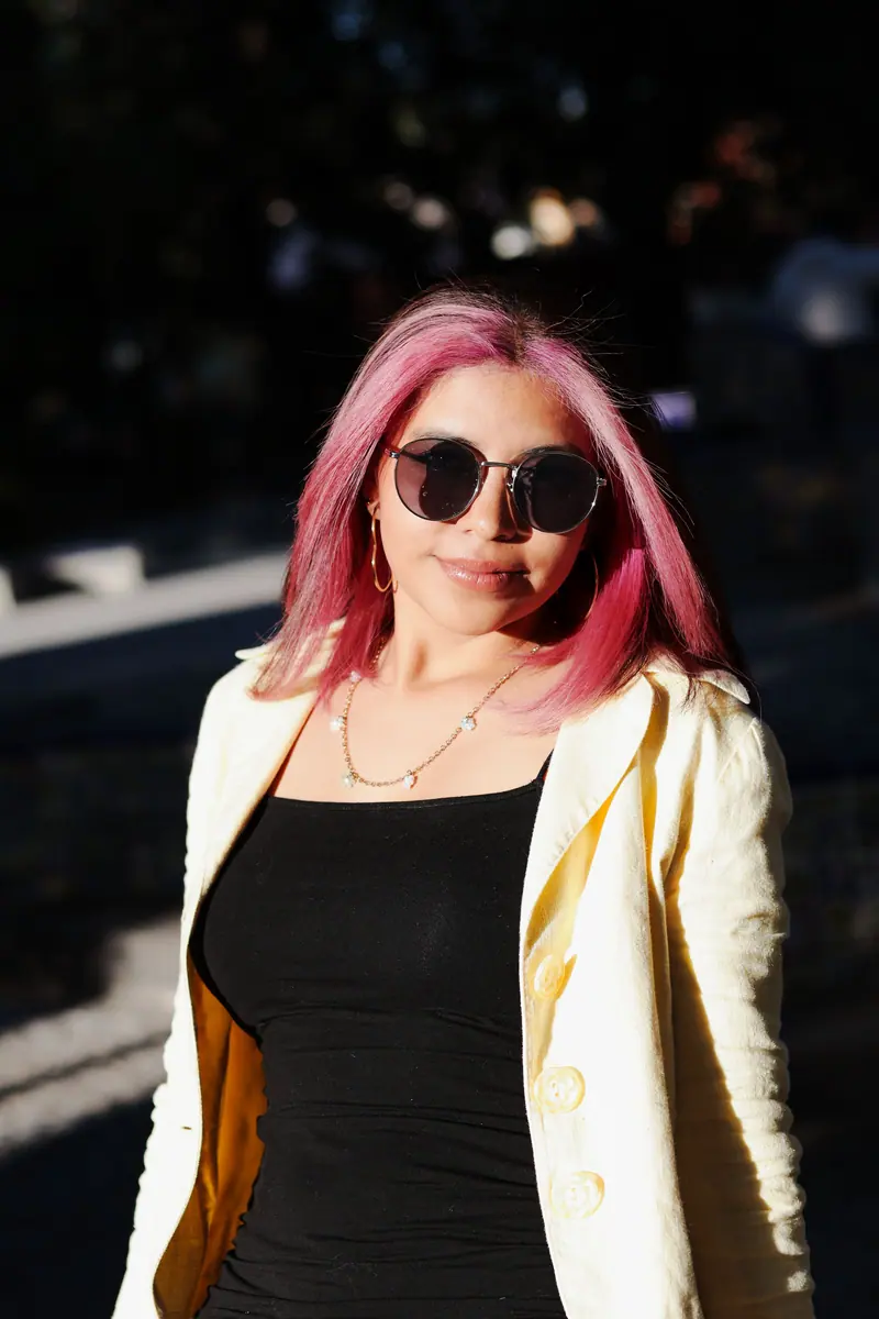 Fashionable woman with pink hair and sunglasses in bright sunlight.