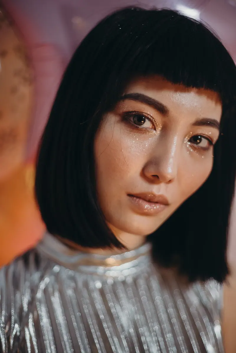 Close-up portrait of a woman with shimmering makeup and sleek hairstyle, dressed in metallic attire.