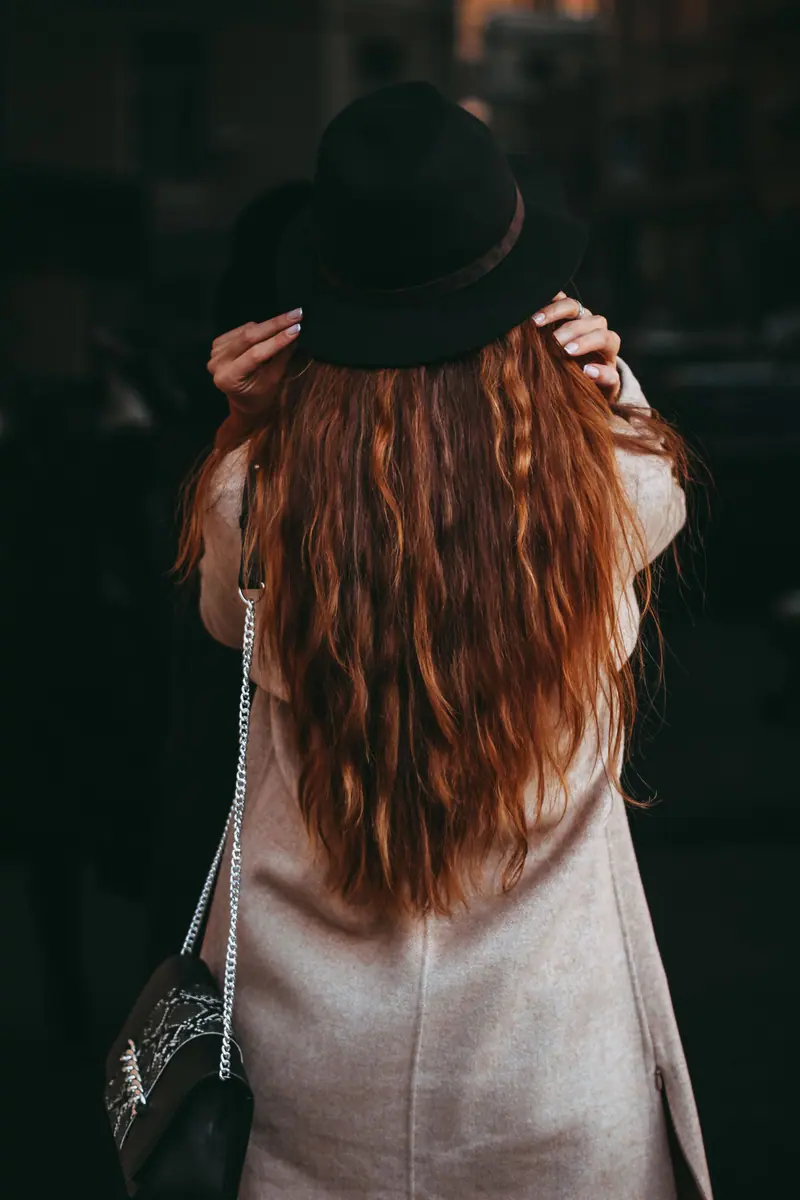 Portrait of a woman with long hair wearing a hat and elegant coat, captured from behind.