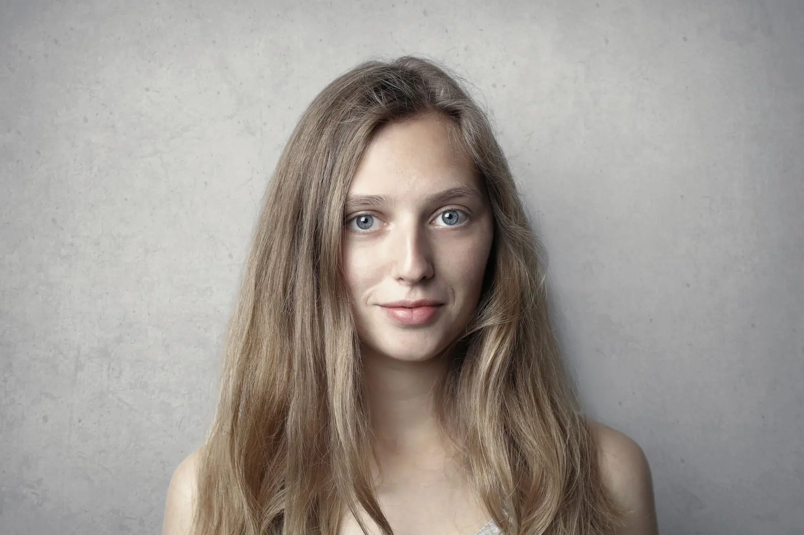 Woman with long natural light-brown hair against a pale stone wall