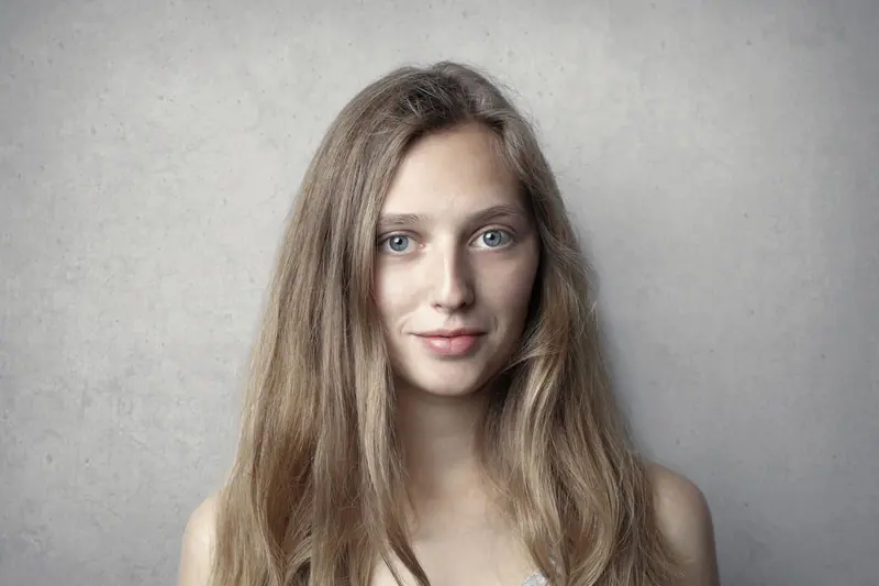 Close-up portrait of a smiling woman with long blonde hair against a gray background.