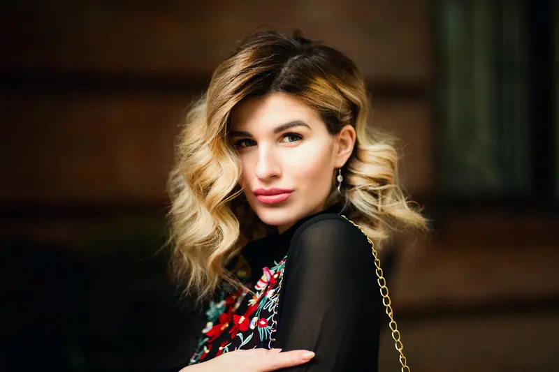 Portrait of a stylish woman outdoors with chic jewelry, soft curls, and a confident look.