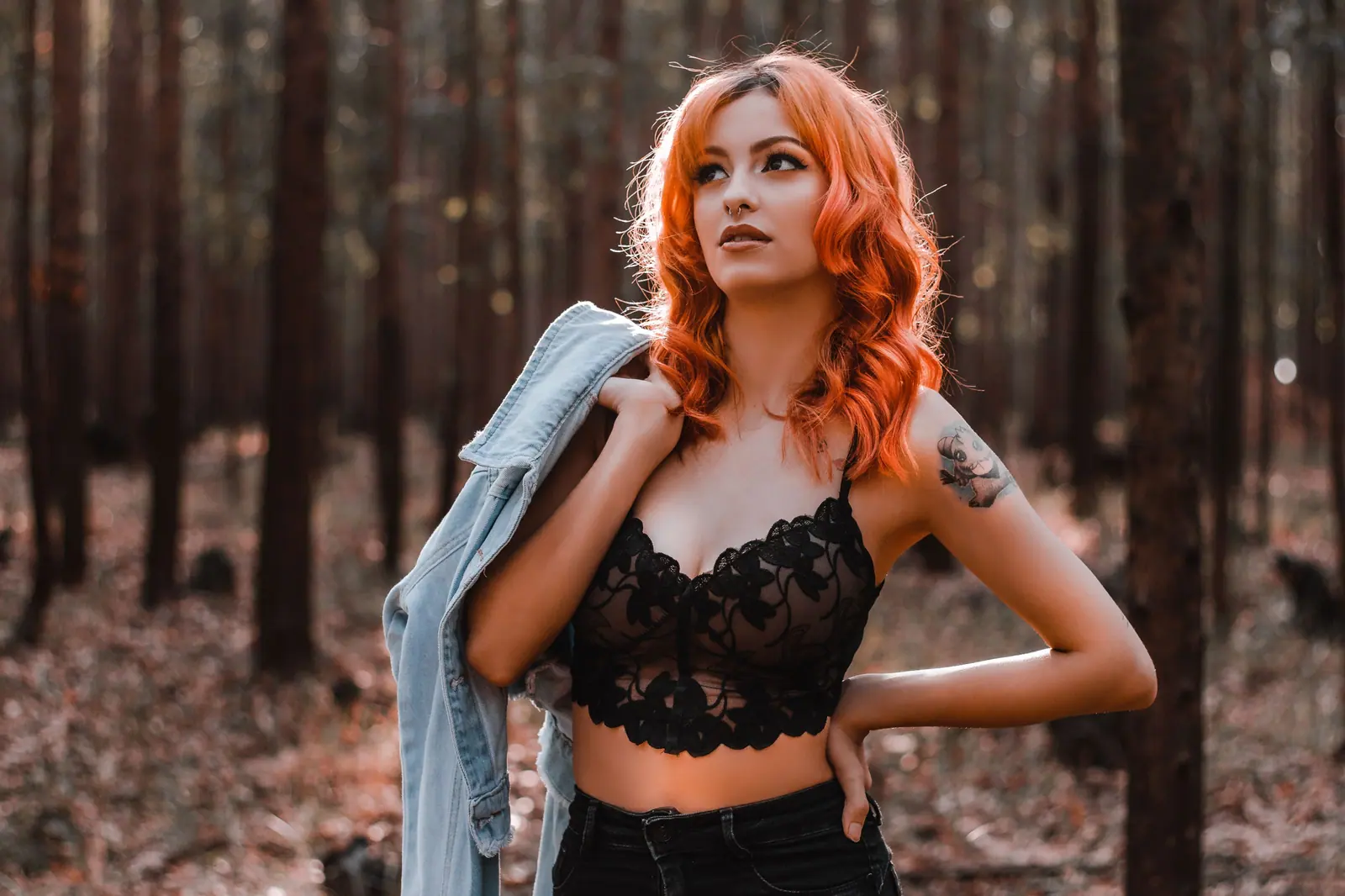 Woman with long copper-red waves in a lace top, standing in a pine forest
