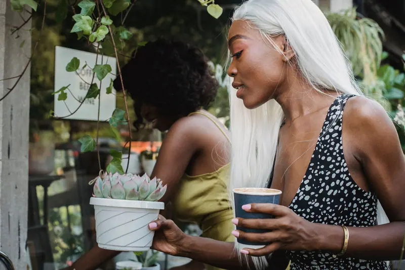 Two women enjoying time outdoors with a succulent and coffee, showcasing a plant-friendly lifestyle.
