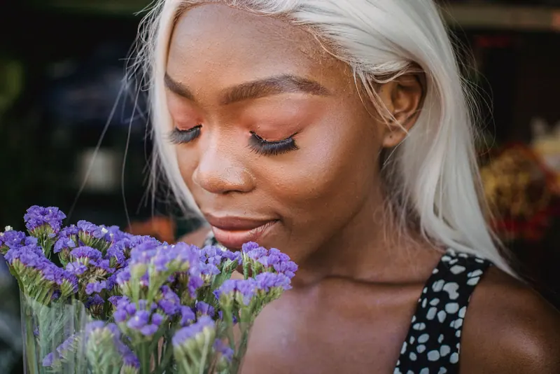 Portrait of a woman with white hair enjoying purple flowers outdoors.