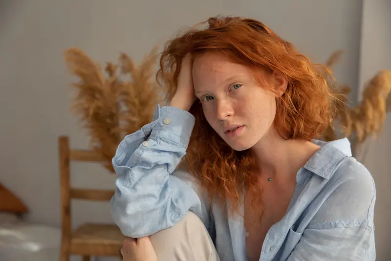 A serene portrait of a red-haired woman leaning on her hand, captured in a tranquil indoor setting.