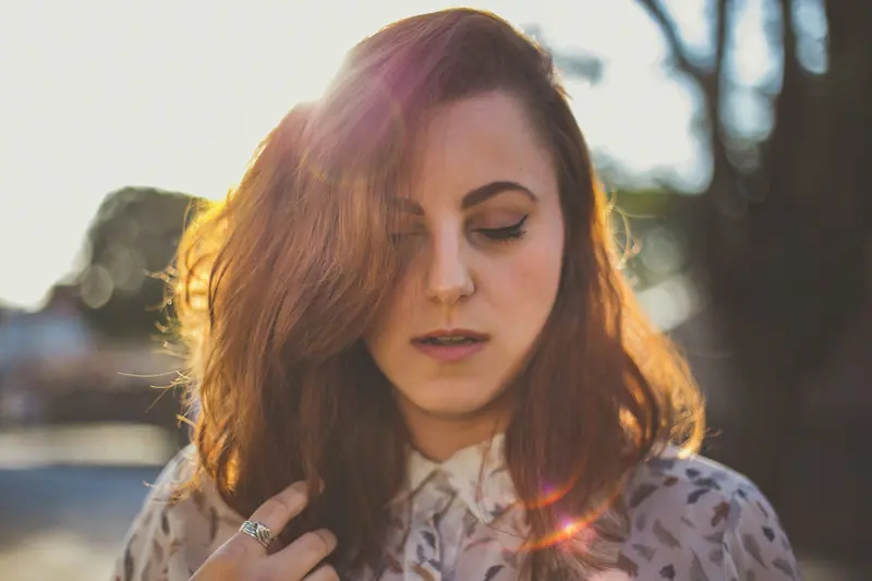 Close-up portrait of a woman with sunlight and lens flare outdoors.
