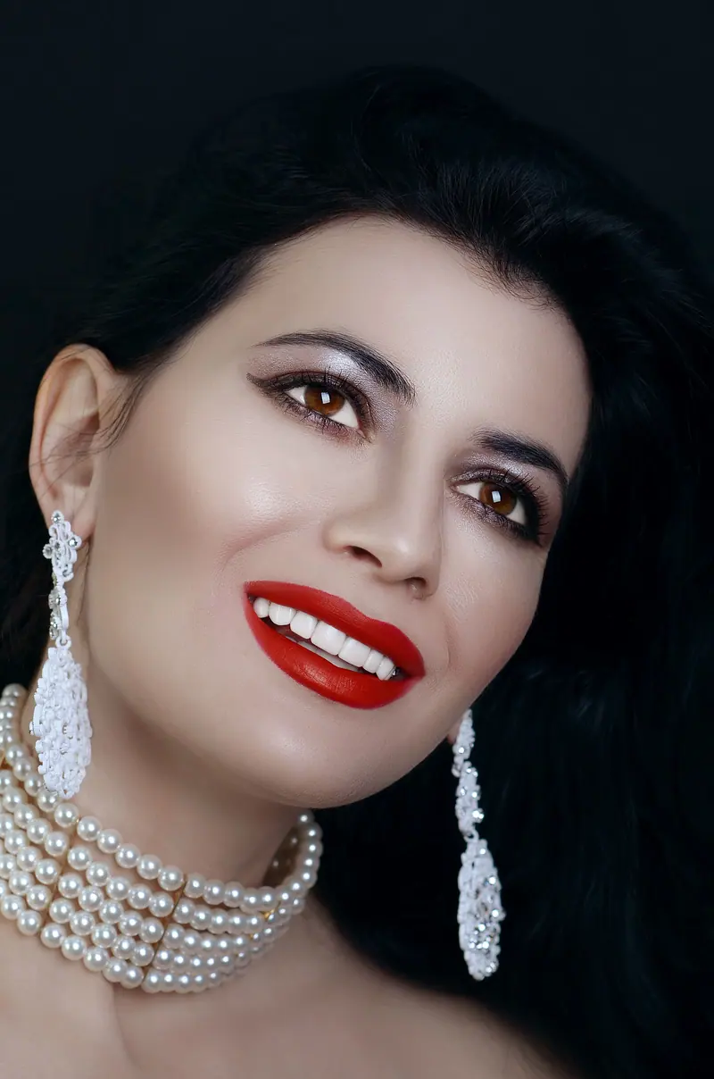 Portrait of a stylish woman with red lips, elegant jewelry, and a captivating smile in a studio setting.