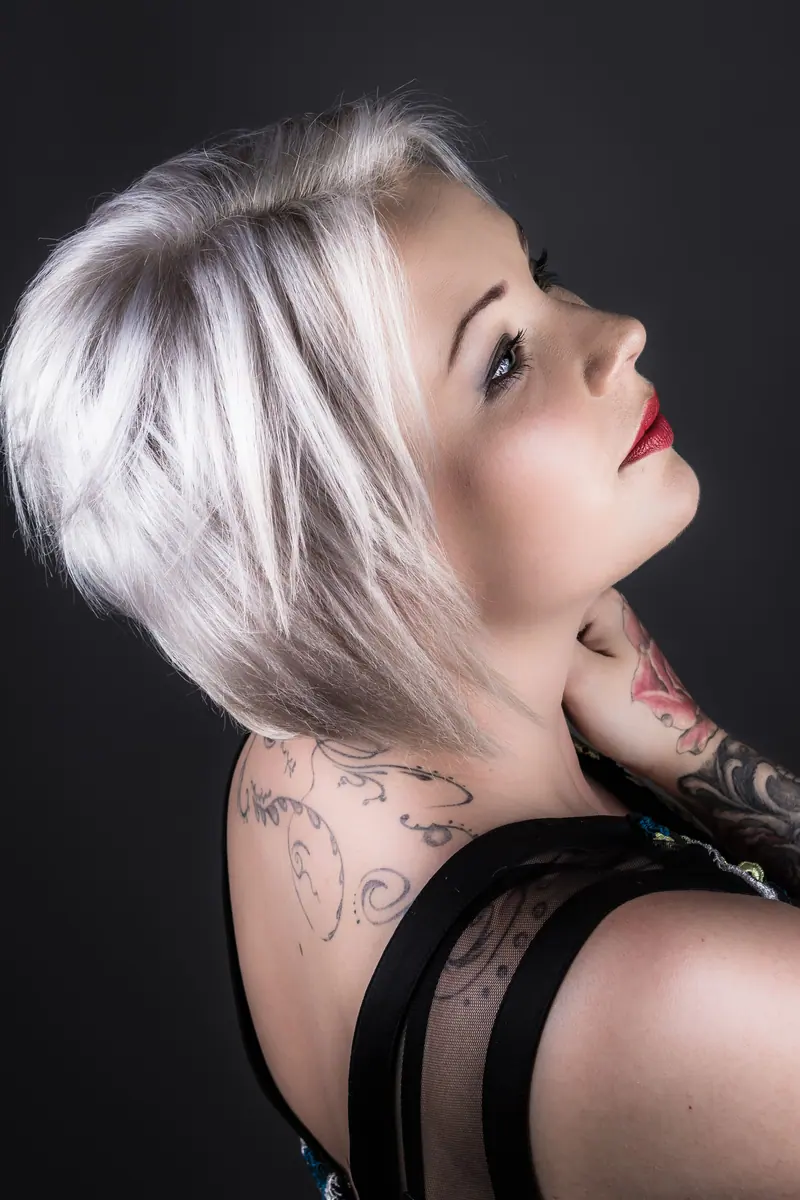 Portrait of a tattooed woman with platinum blonde hair posing in a studio setting, showcasing style and elegance.