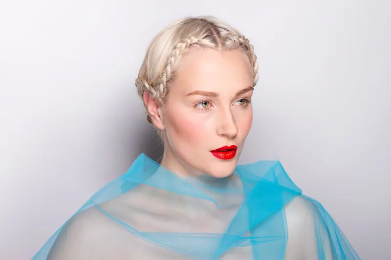 Portrait of a woman with braided hair and red lips against a white background.