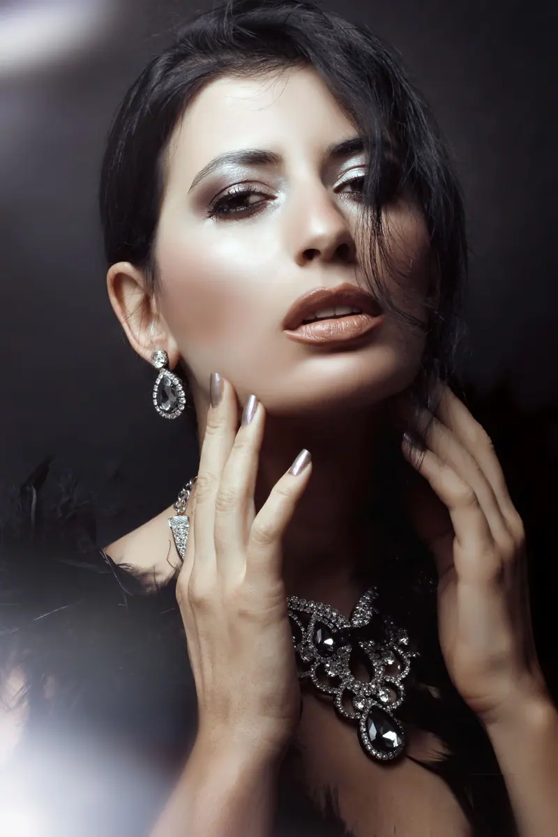 Stunning portrait of a woman showcasing elegant jewelry and makeup indoors.