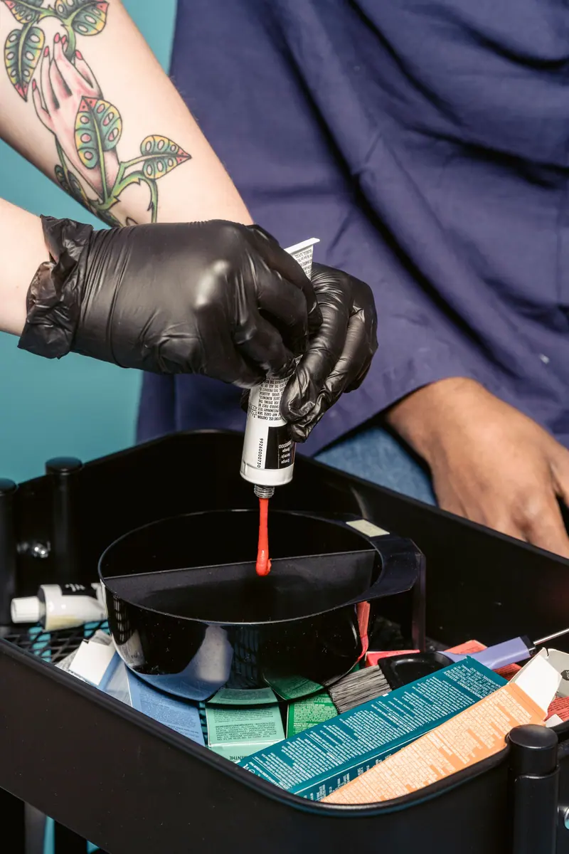 A hairstylist wearing gloves prepares vibrant hair dye in a salon setting.