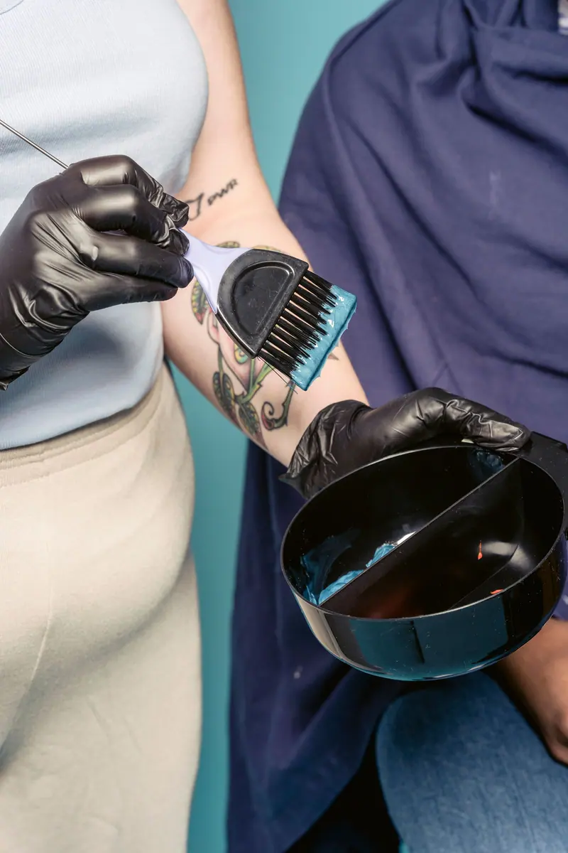 A hairstylist mixes blue hair dye with a brush and bowl inside a salon.