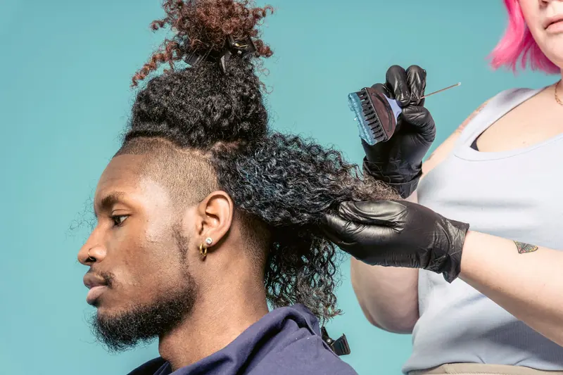 A hairstylist applies dye to a man's curly hair in a studio setting, showcasing professional hairdressing skills.